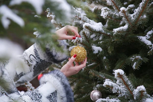 Woman decorating outdoor Christmas tree with golden Christmas bubble. Holidays and winter concept.