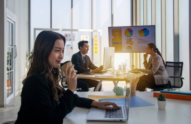 Samimi bir çalışma ortamı. Başarılı gülümseyen iş kadını masada oturmuş defter üzerinde çalışıyor ve iki iş adamının arka planında kahve fincanı tutuyor..