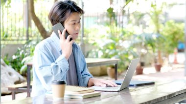 Evde çalışan, cep telefonu kullanan mutlu Asyalı genç adam, akıllı telefon, insan ve teknoloji kullanırken gülümseyen Asyalı erkek, e-ticaret, çevrimiçi iş, e-öğrenme, eğitim, yaşam tarzı kavramı