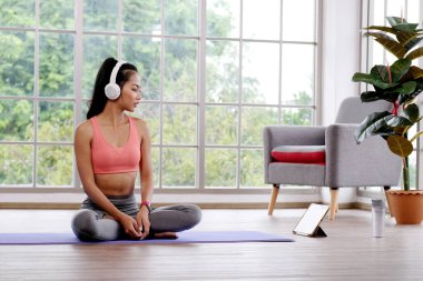 Evde online eğitim kursu, sağlıklı Asyalı kadın oturma odasında dijital tabletle spor yaparken vücudunu esnetiyor.