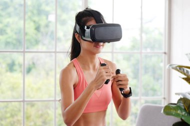 Asyalı kadın sanal gerçeklik kulaklığı evde egzersiz yaparken sağlıklı Asyalı kız interaktif egzersiz, spor, kadın ve giyilebilir teknoloji için VR gözlük takıyor.
