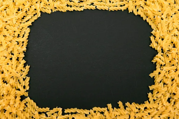 Рамка из сырой пасты Фузилли, разбросанной по черному столу — стоковое фото