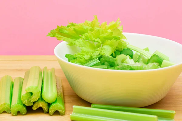 Fresh Chopped Celery Slices in White Bowl with Celery Sticks on Bamboo Cutting Board