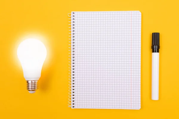 Lámpara de ahorro de energía brillante con bloc de notas acostado en la mesa amarilla — Foto de Stock