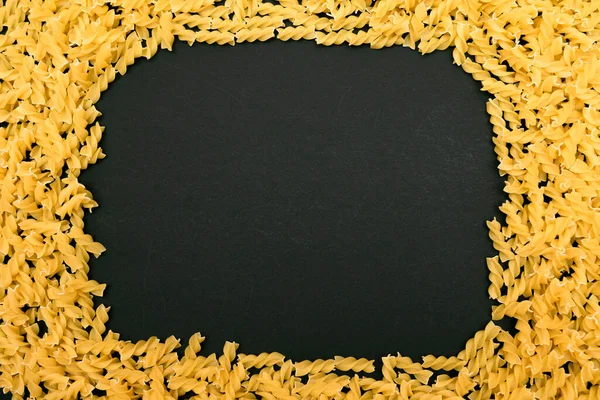 A Frame Made from Uncooked Fusilli Pasta Scattered on Black Table — Stock Photo, Image