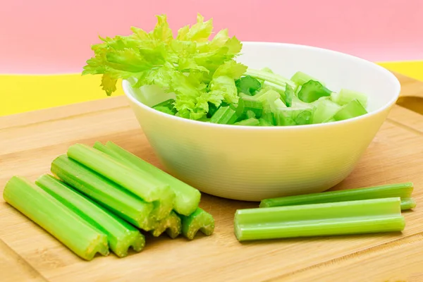 Fresh Chopped Celery Slices in White Bowl with Celery Sticks on Bamboo Cutting Board