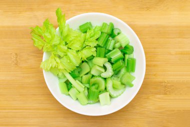 Bambu kesme tahtasında taze doğranmış kereviz dilimleri beyaz kasede - üst görünüm