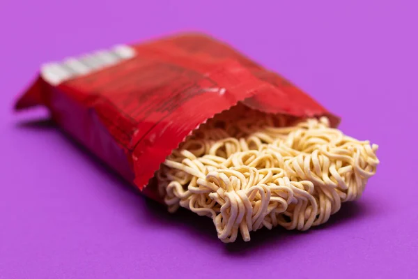 Opened Package with Uncooked Instant Noodles on Violet Background