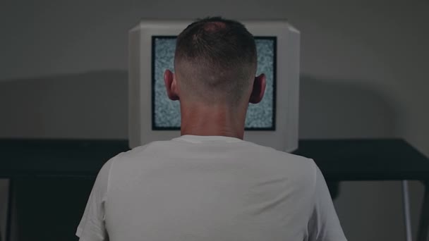 Зомбіфікований чоловік у білій футболці сидить проти старого срібного телевізора — стокове відео