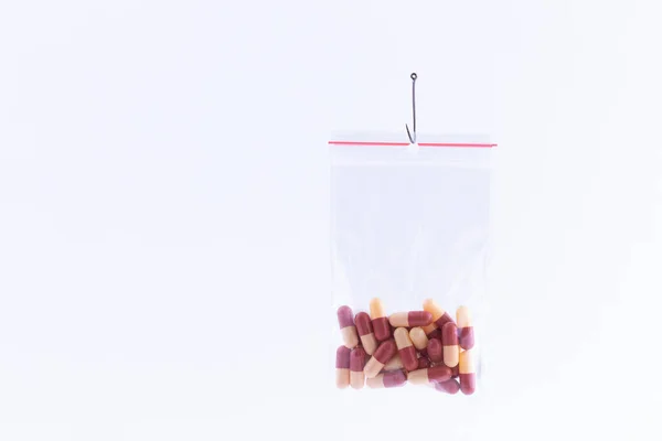 Farbige Pillen oder Tabletten hängen in einer kleinen Reißverschlusstasche am Angelhaken — Stockfoto