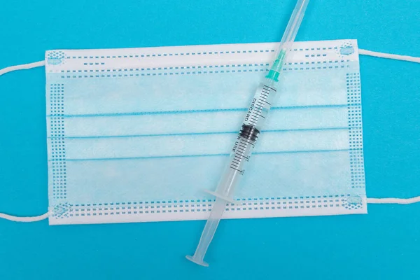 Injekční stříkačka s lékařskou maskou na modrém stole - ploché položit — Stock fotografie