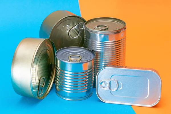 Un grupo de latas apiladas con bordes en blanco sobre fondo azul y naranja Fotos De Stock