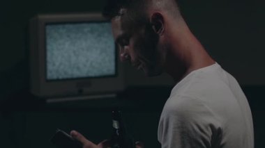 Beyaz tişörtlü adam Eski Gümüş TV karşısında oturuyor.