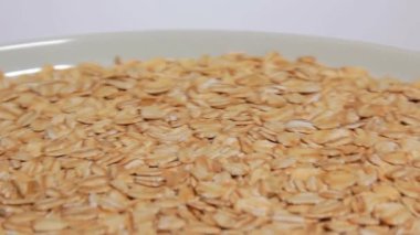 Pişmemiş Yulaf Gevreği Beyaz Plaka 'da Beyaz Arkaplan' a karşı dönüyor. Dağıtılmış Kuru ve Çiğ Yulaf Gevreği. Sağlıklı Kahvaltı ve Beslenme Malzemeleri