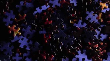 Background of Colored Puzzle Pieces that Slowly Rotating Counterclockwise - Top View. Texture of Incomplete Red and Blue Jigsaw Puzzle with Low Key Light - Left Rotation