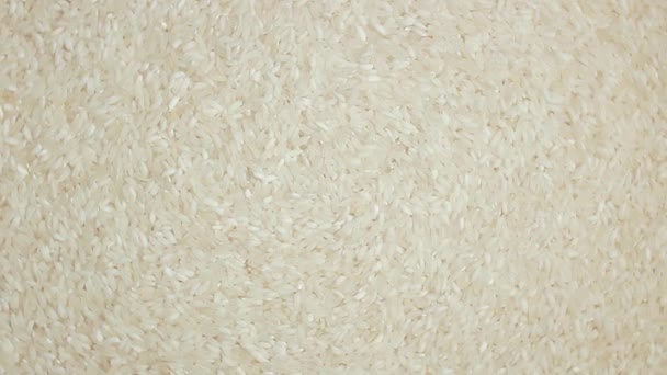 乾燥調理されていない白米の背景をゆっくりと右回転 トップビュー 生の長粒米を散布 アジア料理と文化 健康的な食材 — ストック動画