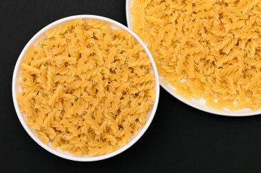 Pişmemiş Fusilli Makarna Siyah Arkaplanda Beyaz Tabakta Yatıyor. Çiğ ve kuru makarna. Sağlıksız ve Yağlı Gıda - Üst Görünüm