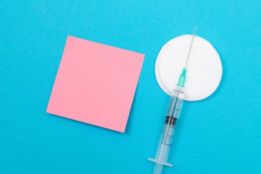 Aşı, Bağışıklık Bilimi veya Yeniden Aşılama Konsepti - Bir Hastane veya Klinikte Mavi Masa üzerinde yatan Tıbbi Tek Kullanılabilir Şırınga. Boş Pembe Yapışkan Not - Uzayı Kopyala ile Moklonla