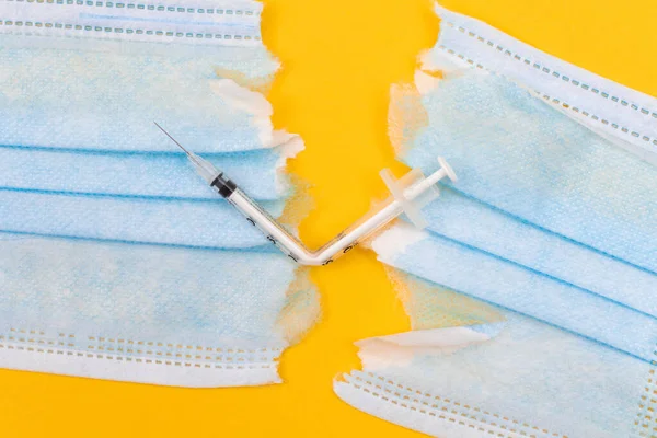 Anti Vaccine Movement and Anti Mask Concept - Broken Medical Syringe and Torn Medical Face Mask Lying on Yellow Background. Pandemic and Lockdown End - Top View, Flat Lay