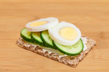 Bambu kesme tahtasında taze salatalık, yumurta, krem peynir ve turplu tam tahıllı gevrek. Kolay Kahvaltı 'da. Hızlı ve sağlıklı sandviçler. Lezzetli dolgulu kızarmış ekmek. Sağlıklı Beslenme Atıştırması