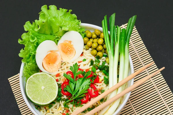 Beautiful Noodle Dish with Green Onions, Eggs, Red Hot Pepper, Greens and Lime on Sushi Mat. Instant Noodles - Top View