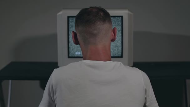 壊れたテレビやテレビ宣伝 白いTシャツのゾンビ男は暗い部屋の古いシルバーテレビに対して座っています テレビ信号を検索しましょう 画面上の歪み ビュー 静的ショット フィルム穀物 — ストック動画