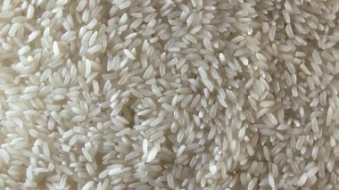 Dry Uncooked White Rice Background Slowly Rotating Right - Top View, Low Key Light. Scattered Raw Long Grain Rice. Asian Cuisine and Culture. Healthy Eating Ingredients. Diet Food