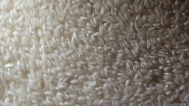 Kuru, pişmemiş, beyaz pirinç arka planı sola doğru dönüyor. Çiğ Uzun Taneli Pirinç. Asya mutfağı ve kültürü. Sağlıklı beslenme malzemeleri. Diyet yemek. Açısal Döndürme Saat Yönünün Tersine