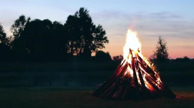 Big Burning Campfire at Summer Evening against the Blue Sky. Wood on Fire. Flying Sparks. Travel and Tourism Concept. Giant Flaming Bonfire - Static Shot, Timelapse
