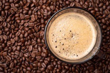 Kahve fincanının en üst görüntüsü ve bir grup siyah kahve çekirdeği arka plandadır. Koyu siyah espresso, kahve arkaplanı, doku.