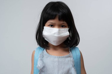 Koruyucu maskeli ve okul çantalı Asyalı kız çocuğu portresi. Yeni okul yılına pandemik kısıtlamalarla hazır. Çocuğun okula geri dönmesi ve yeni normal yaşam tarzı.