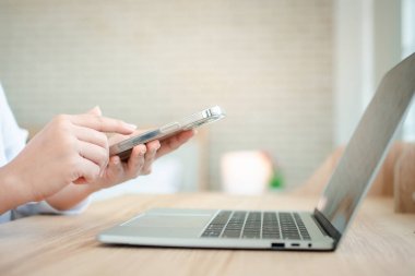 Laptop ve akıllı telefonla çalışan mutlu Asyalı kadın. Ofiste masada oturuyor. Not defteri ve akıllı telefon kavramını kullanarak çevrimiçi mutlu kadın profesyonel serbest yazar.