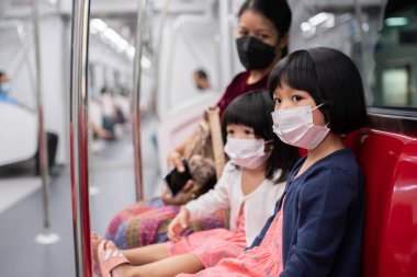 Cerrahi maskeli küçük kız, toplu taşımada (hava treni veya metro) koruma gribi ve virüs salgınıyla karşı karşıya. Yeni normal yaşam tarzı kavramı, okula gitmek için toplu taşıma araçlarını kullanmak..