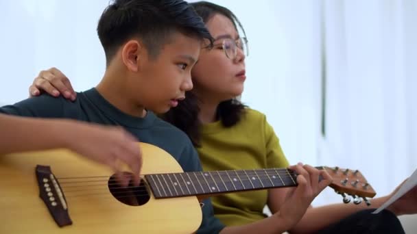 アジアの母親は息子を包含し アジアの少年はギターを演奏し 母親はソファに抱擁し 感謝し 奨励しています 幸せな家族 楽しいライフスタイル 家族の絆の概念 — ストック動画