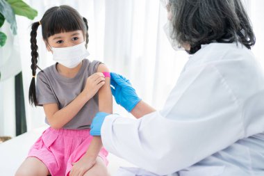 Doktor, hastanedeki Asyalı kızların omzuna aşılandıktan sonra tıbbi sıvayı yapıştırıyor. Pediyatrist çocuklar için aşı yapıyor. Aşılama, aşılama, hastalık önleme kavramı.