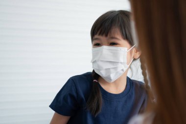 Asyalı aileler okula gitmeden önce Coronavirus covid 19 'a karşı korunmak için küçük kızlarına yüz maskesi takarlar. Annesi kızına tıbbi maske takmasını öğretiyor.