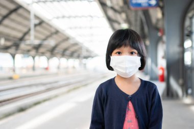 Cerrahi maskeli küçük kız, toplu taşımada (hava treni veya metro) koruma gribi ve virüs salgınıyla karşı karşıya. Yeni normal yaşam tarzı kavramı, okula gitmek için toplu taşıma araçlarını kullanmak..