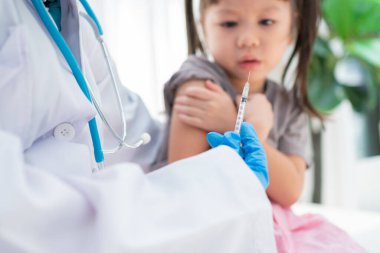 Hastanedeki Asyalı kızların omzunda aşı yapmak için şırınga tutan doktor. Pediyatrist çocuklar için aşı yapıyor. Aşılama, aşılama, hastalık önleme kavramı.