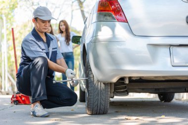 Üniformalı uzman bir tamirci, vidaları sökmeye çalışıyor vidaları sökmeye çalışıyor ve otoyolda tekerlek değiştiren bir kadına yardım ediyor, araba servisi, onarım, bakım konsepti....