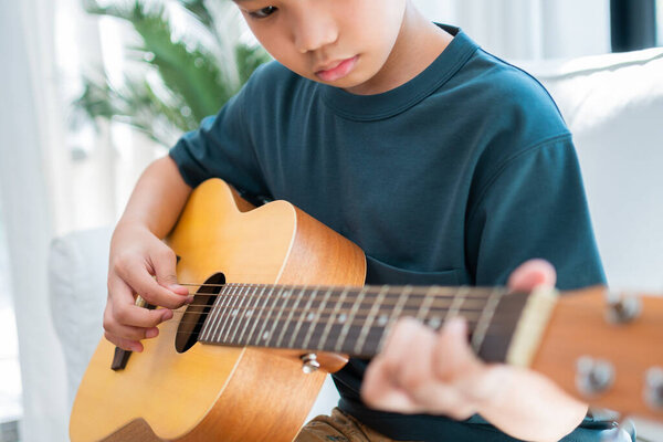Asian boy playing guitar with father in the living room for teaching him son play guitar, feel appreciated and encouraged. Concept of a happy family, learning and fun lifestyle, love family ties