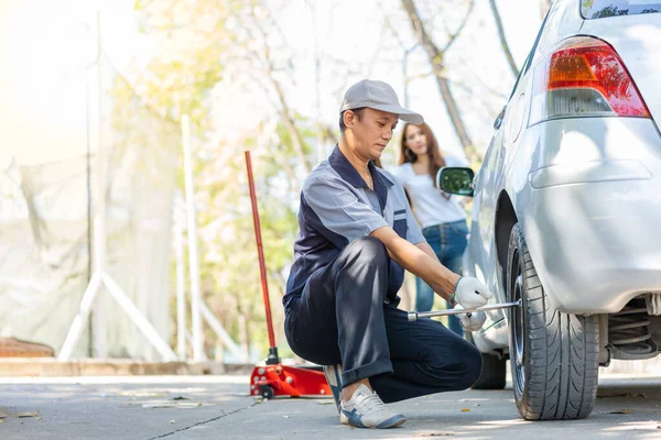 Expertise mechanic man  in uniform using force trying to unscrew the wheel bolts nuts and help a woman for changing car wheel on the highway, car service, repair, maintenance concept.