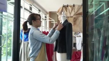 Mutlu Asyalı kadın terzi moda tasarımcısı bir elbise ve galeride elbise için hazırlık yapıyor. Başarı kavramı Moda sektöründeki genç girişimci.