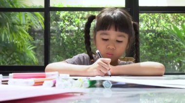 Renkli kalem çekip resim yapan sevimli Asyalı kız eğleniyor ve gülüyor. Yaratıcı hobi ve çocuk gelişimi kavramı.