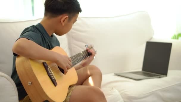 亚洲男孩在虚拟会议上学习弹吉他 以便与朋友或老师一起在网上用笔记本电脑举行的视频会议上演奏音乐 — 图库视频影像
