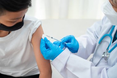 Hastanedeki Asyalı çocukların omzunda aşı yapmak için şırınga tutan doktor. Pediyatrist çocuklar için aşı yapıyor. Aşılama, aşılama, hastalık önleme kavramı.