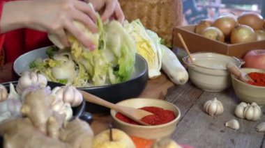 Geleneksel Kore kıyafetleri giyen Asyalı kadınlar, sarımsak, gochugaru (Kore biberi) ve taze sebze gibi malzemelerle el yapımı tuz ve Kimchi malzemeleri serpiyorlar..
