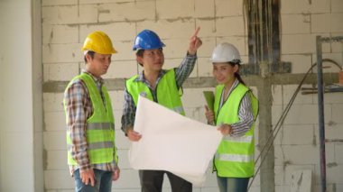 Bir grup Asyalı mühendis ya da genç bayan mimar güvenlik için bir kask taktılar ve bir inşaat fabrikası projesi için müteahhitle görüştüler: Takım çalışması kavramı, liderlik kavramı..