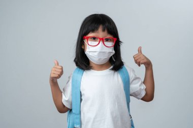 Korumacı yüz maskeli, okul çantalı ve yeni okul yılına hazır Asyalı bir kızın portresi. Çocuğun okula geri dönmesi ve yeni normal yaşam tarzı.