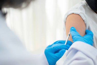 Hastanedeki Asyalı çocukların omzunda aşı yapmak için şırınga tutan doktor. Pediyatrist çocuklar için aşı yapıyor. Aşılama, aşılama, hastalık önleme kavramı.