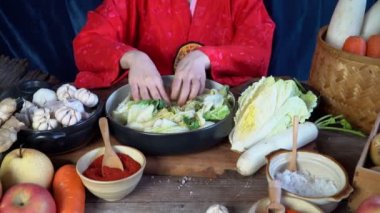 Geleneksel Kore kıyafetleri giyen Asyalı kadınlar, sarımsak, gochugaru (Kore biberi) ve taze sebze gibi malzemelerle el yapımı tuz ve Kimchi malzemeleri serpiyorlar..